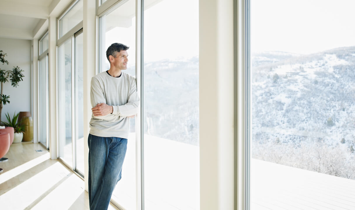 A man wearing a white sweater looking out the window.